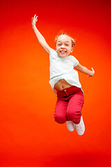 Image showing Young happy caucasian teen girl jumping in the air, isolated on red studio background.