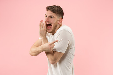 Image showing The young man whispering a secret behind her hand over pink background