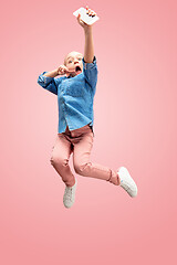 Image showing Young happy caucasian teen girl jumping with phone in the air, isolated on pink studio background.