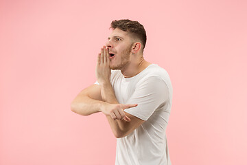 Image showing The young man whispering a secret behind her hand over pink background