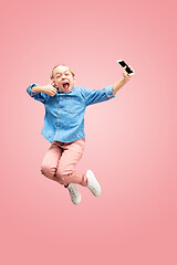 Image showing Young happy caucasian teen girl jumping with phone in the air, isolated on pink studio background.