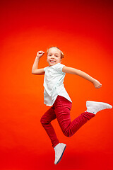 Image showing Young happy caucasian teen girl jumping in the air, isolated on red studio background.