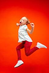 Image showing Young happy caucasian teen girl jumping in the air, isolated on red studio background.