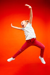 Image showing Young happy caucasian teen girl jumping in the air, isolated on red studio background.