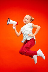 Image showing Beautiful young child teen girl jumping with megaphone isolated over red background