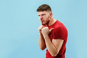 Image showing The young man whispering a secret behind her hand over blue background