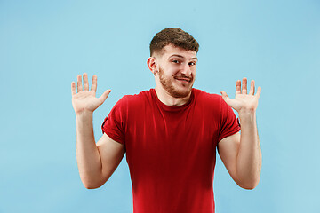 Image showing Beautiful male half-length portrait isolated on blue studio backgroud. The young emotional surprised man