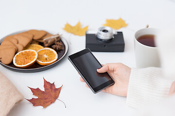 Image showing hand with smartphone, tea and autumn leaves