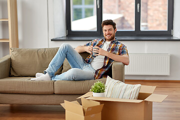 Image showing man with boxes and drinking coffee at new home