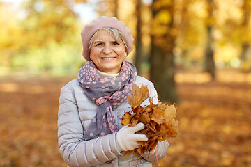 Image showing senior woman with maple leaves at autumn park