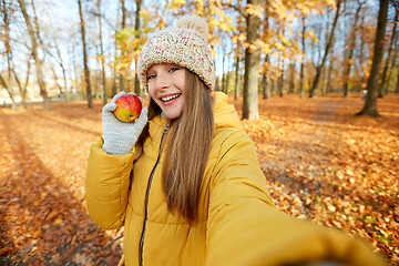 Image showing happy girl with apple taking selfie at autumn park