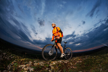 Image showing cyclist standing with mountain bike on trail at sunset