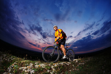 Image showing cyclist standing with mountain bike on trail at sunset