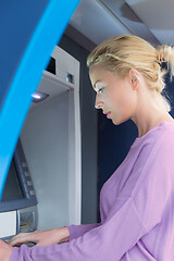 Image showing Young lady withdrawing money at ATM machine entering her pin code.