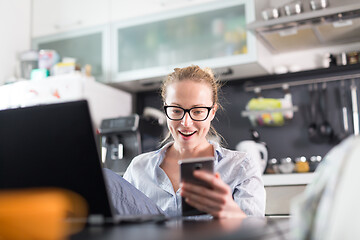 Image showing Stay at home and social distancing. Woman in her casual home clothing working remotly from kitchen dining table. Video chatting using social media with friend, family, business clients or partners