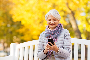 Image showing happy senior woman with smartphone at autumn park