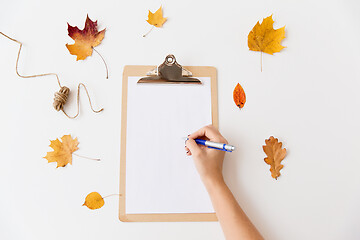 Image showing hand writing on white paper on clipboard in autumn