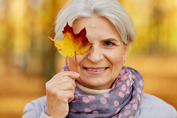 Image showing happy senior woman with maple leaf at autumn park