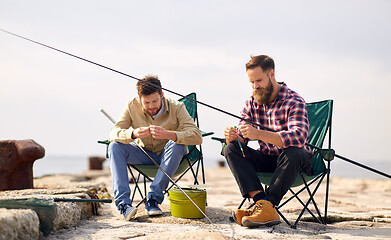 Image showing friends adjusting fishing rods with bait on pier