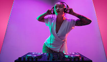 Image showing Young caucasian female musician in headphones performing on purple background in neon light