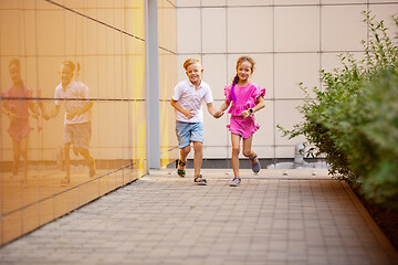 Image showing Two smiling kids, boy and girl running together in town, city in summer day