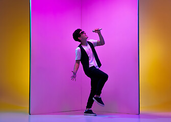 Image showing Young male musician, singer performing on pink-orange background in neon light