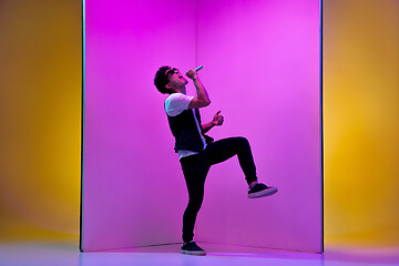 Image showing Young male musician, singer performing on pink-orange background in neon light