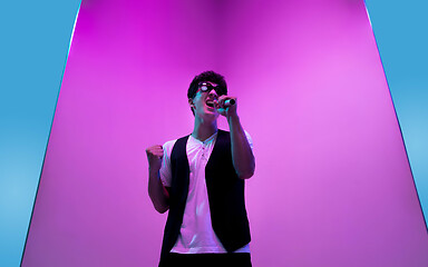 Image showing Young male musician, singer performing on pink-blue background in neon light