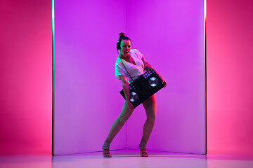 Image showing Young caucasian female musician in headphones performing on purple background in neon light