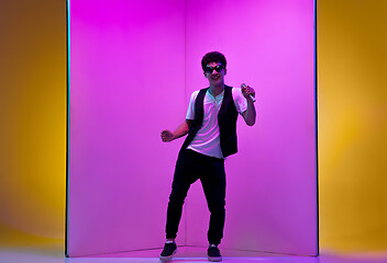 Image showing Young male musician, singer performing on pink-orange background in neon light