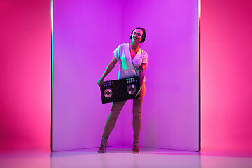 Image showing Young caucasian female musician in headphones performing on purple background in neon light