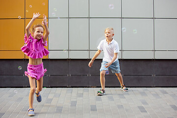 Image showing Two smiling kids, boy and girl running together in town, city in summer day