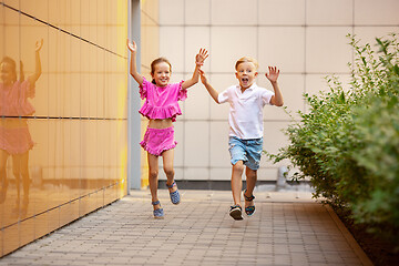 Image showing Two smiling kids, boy and girl running together in town, city in summer day