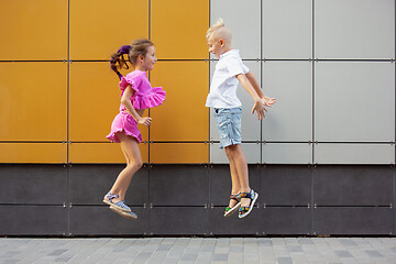 Image showing Two smiling kids, boy and girl running together in town, city in summer day