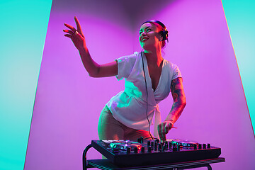 Image showing Young caucasian female musician in headphones performing on purple background in neon light