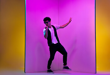 Image showing Young male musician, singer performing on pink-orange background in neon light