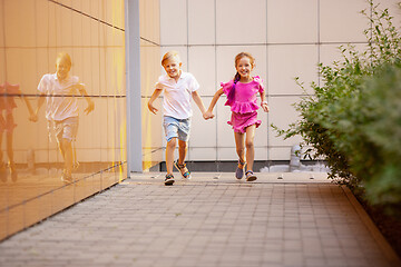 Image showing Two smiling kids, boy and girl running together in town, city in summer day