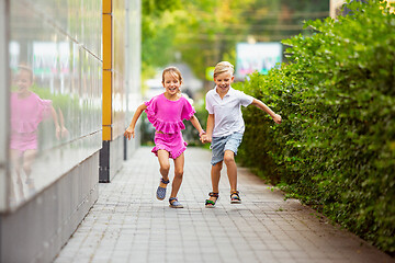 Image showing Two smiling kids, boy and girl running together in town, city in summer day