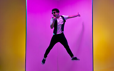 Image showing Young male musician, singer performing on pink-orange background in neon light