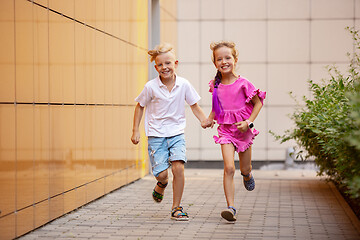 Image showing Two smiling kids, boy and girl running together in town, city in summer day