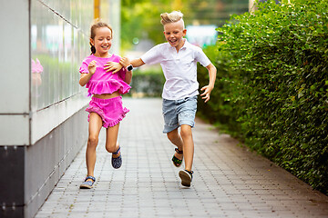 Image showing Two smiling kids, boy and girl running together in town, city in summer day