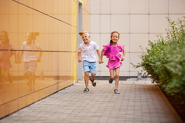 Image showing Two smiling kids, boy and girl running together in town, city in summer day