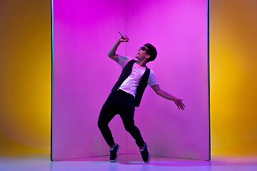 Image showing Young male musician, singer performing on pink-orange background in neon light