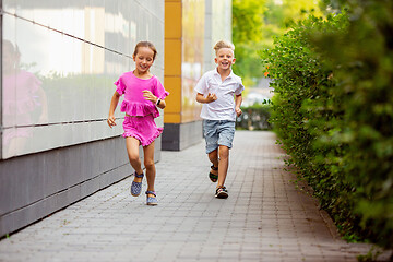 Image showing Two smiling kids, boy and girl running together in town, city in summer day