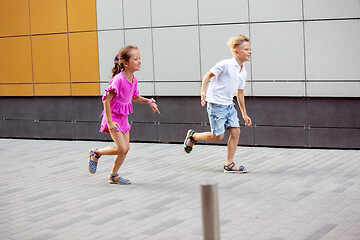 Image showing Two smiling kids, boy and girl running together in town, city in summer day