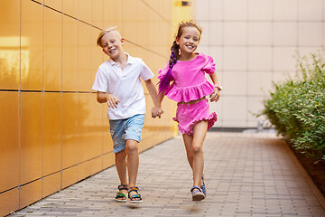 Image showing Two smiling kids, boy and girl running together in town, city in summer day