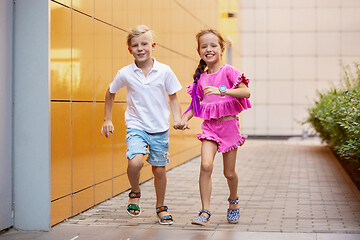 Image showing Two smiling kids, boy and girl running together in town, city in summer day