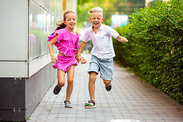 Image showing Two smiling kids, boy and girl running together in town, city in summer day