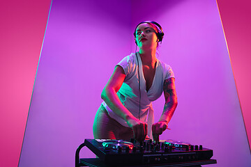 Image showing Young caucasian female musician in headphones performing on purple background in neon light