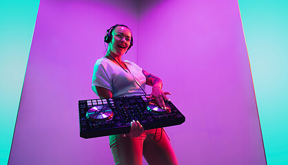 Image showing Young caucasian female musician in headphones performing on purple background in neon light